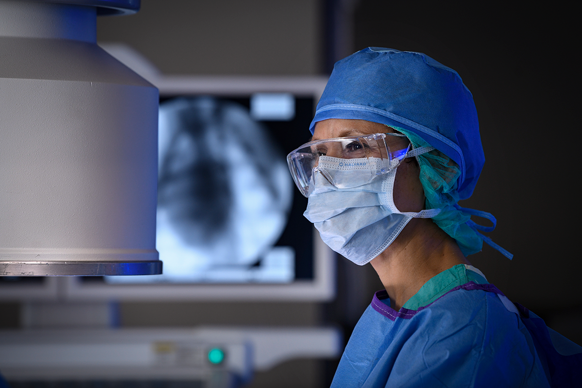 A healthcare worker in a surgical gown and glasses.