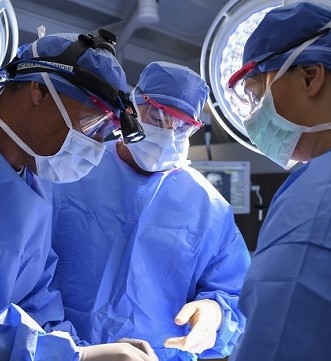 Three surgeons in blue surgical gowns and masks performing a procedure in an operating room.