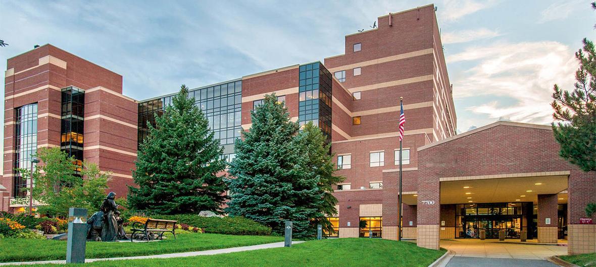 Exterior view of AdventHealth Littleton hospital, a large brick medical facility with a well-maintained lawn and trees in front.